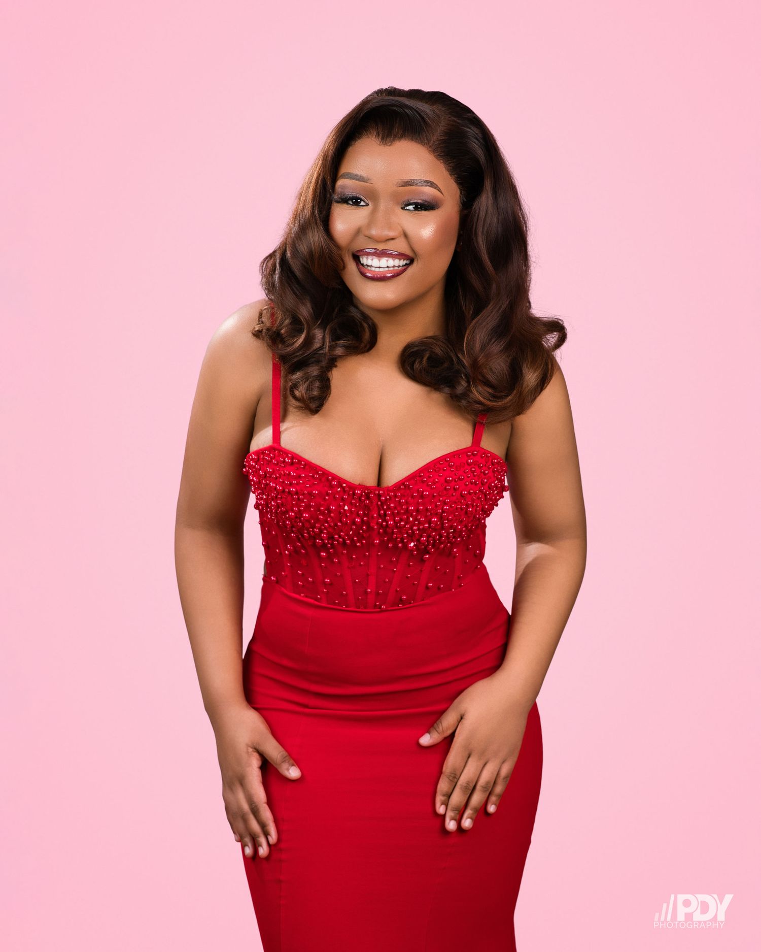 Glamour photography session with red beaded gown against pink background.
