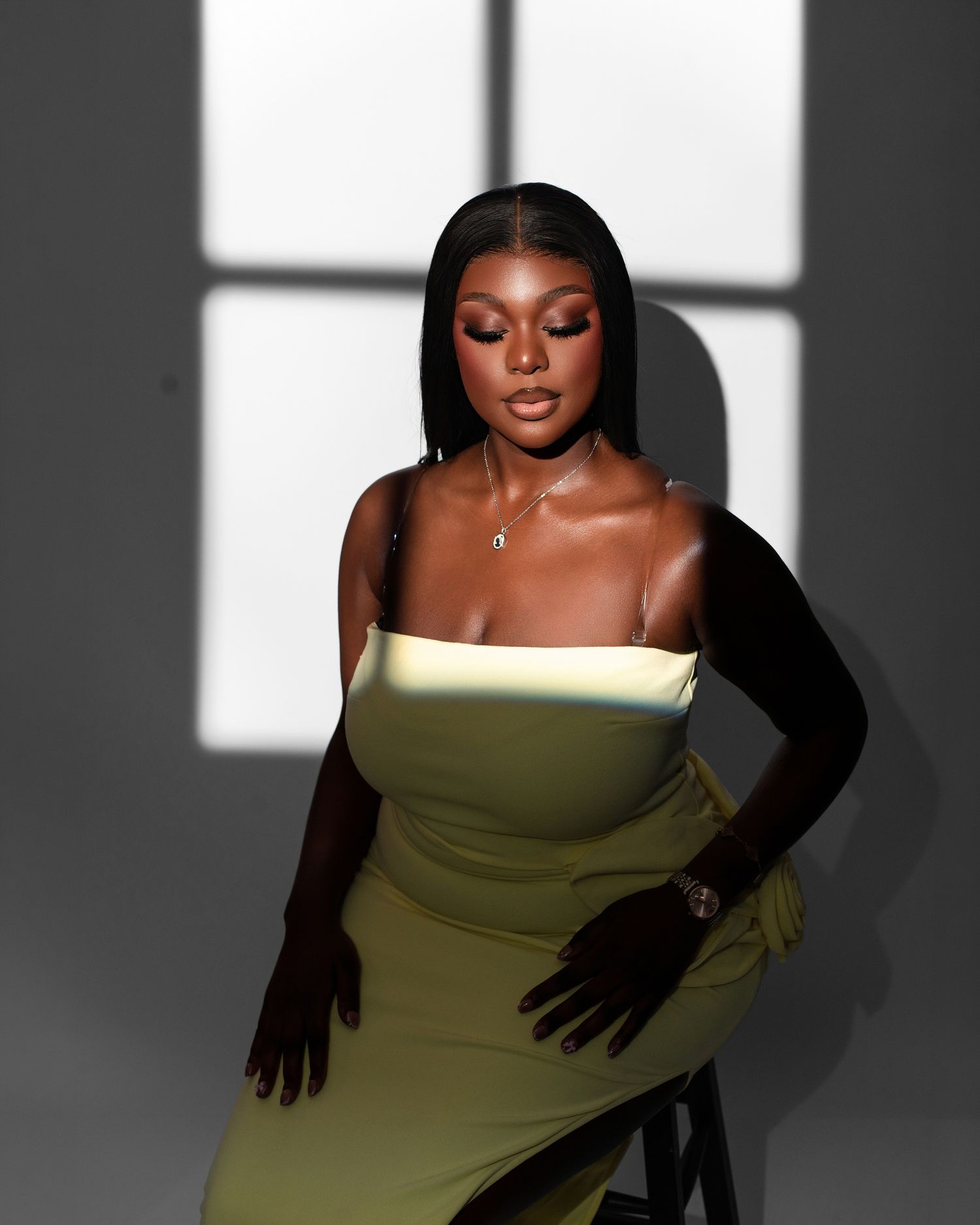 A woman in a lime green strapless dress and long black gloves poses dramatically against a window-lit backdrop.