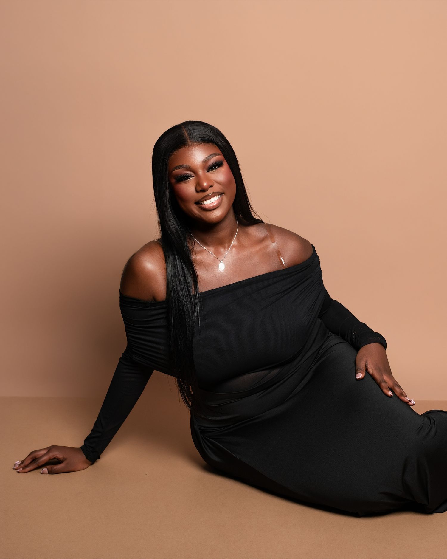 A model in a black off-shoulder dress poses elegantly against a warm brown background.