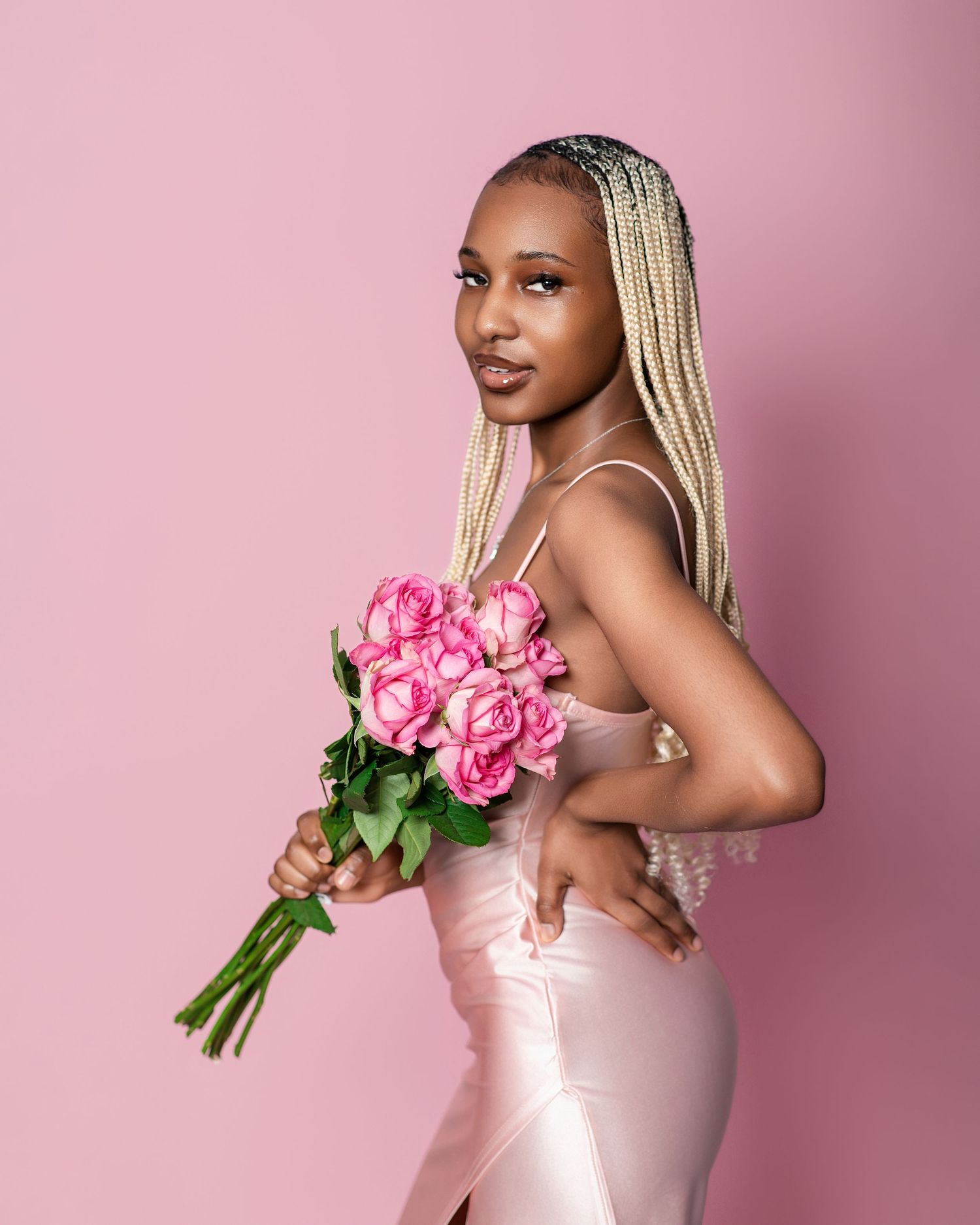 Dynamic pose with pink roses showcasing elegant dress and braided hairstyle.
