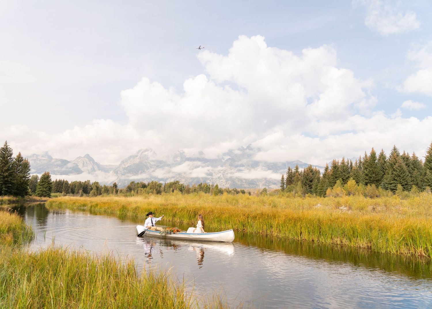 Two canoes navigate through tall grasses on a serene mountain lake under cloudy skies.