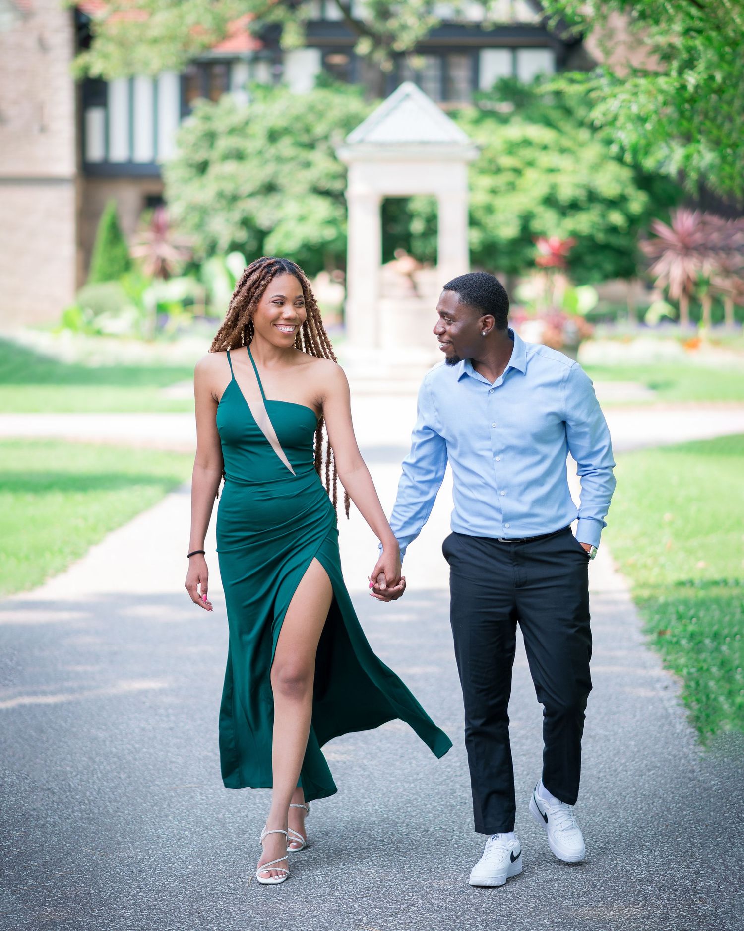 Couple walking and holding hands on a path wearing emerald green dress and light blue shirt.