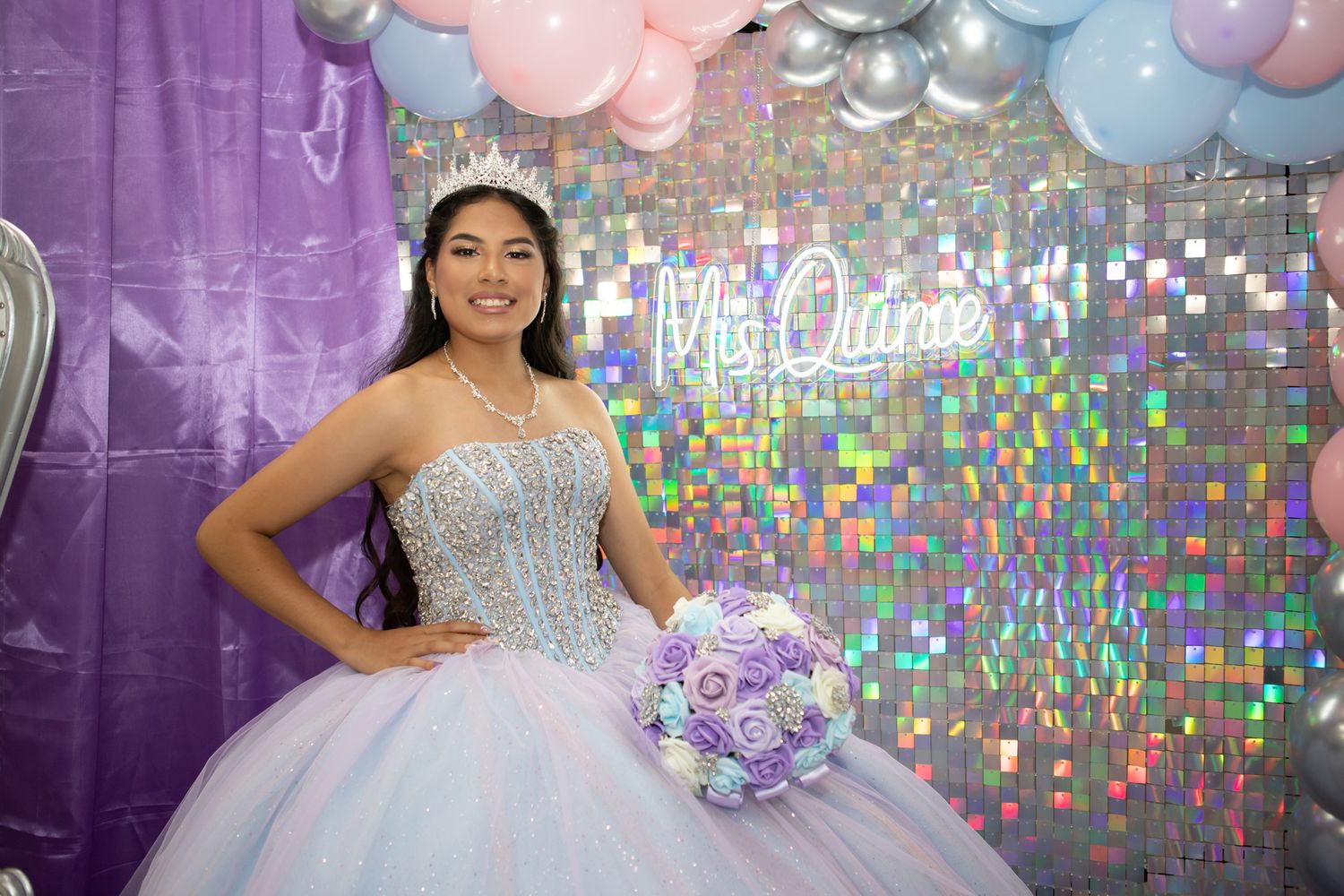 A quinceañera celebration with a sparkly backdrop, purple and pink balloons, and a glittering ball gown.