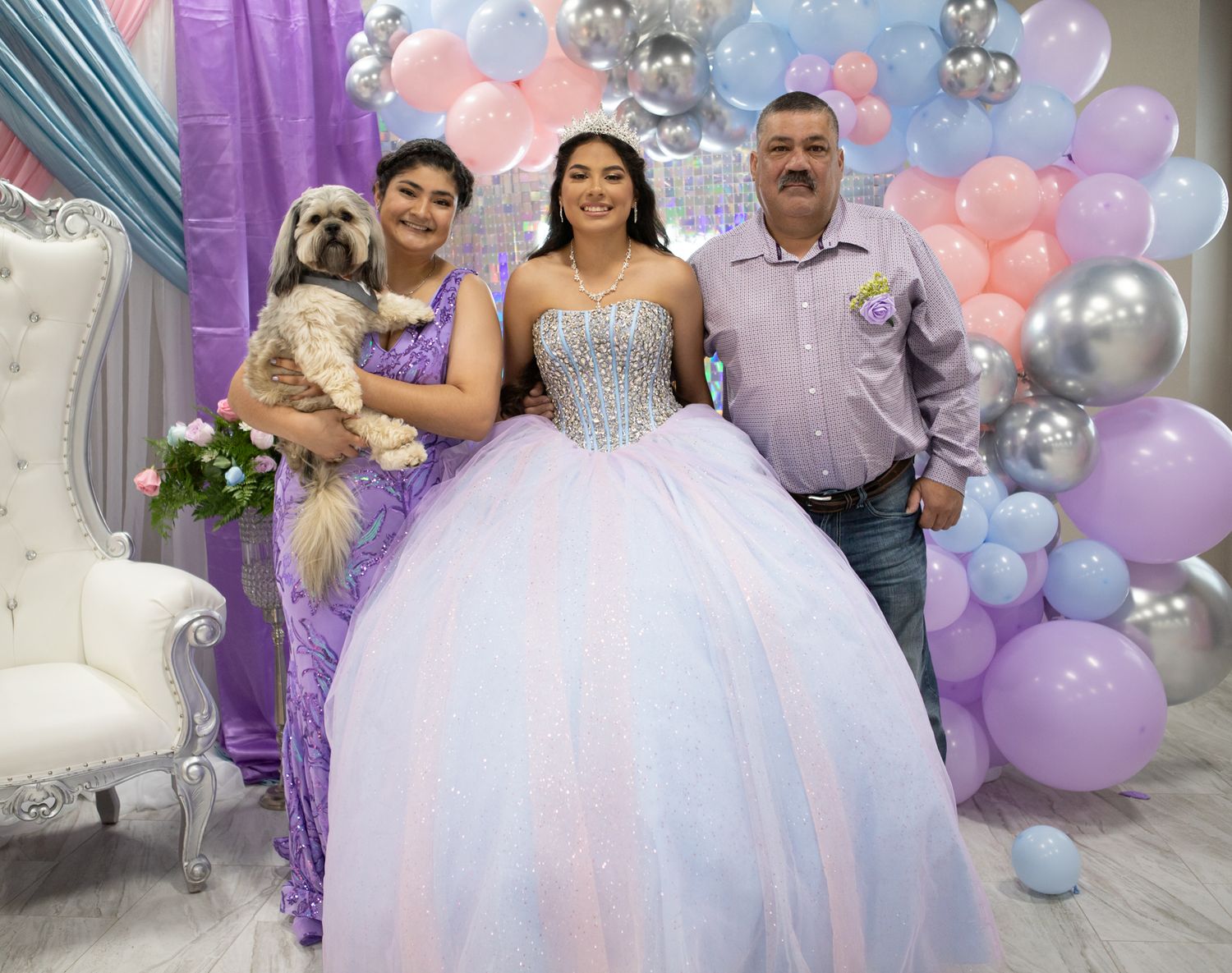 A quinceañera celebration photo with family members and a small dog against a balloon backdrop.