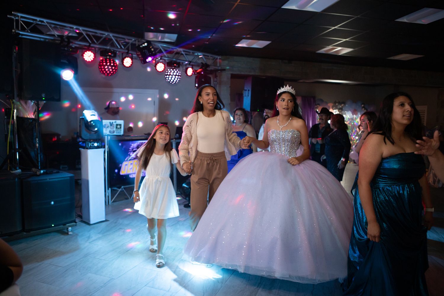 A quinceañera celebration in a dark venue with blue lighting and guests on the dance floor.