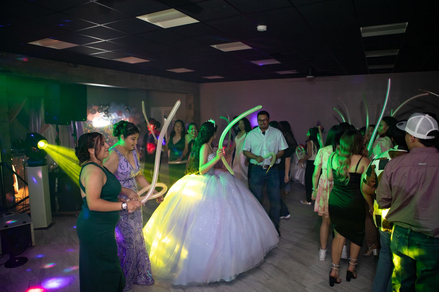 A festive quinceañera dance party with green lighting and guests celebrating on the dance floor.