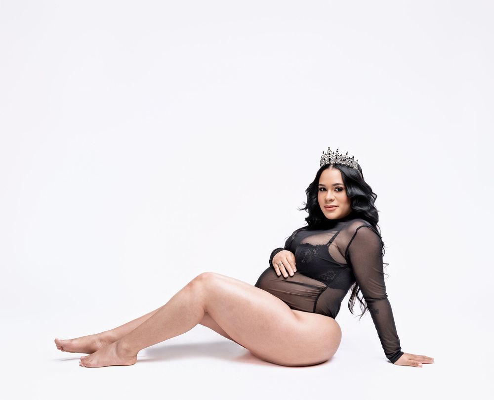 A figure in a sheer black bodysuit with long sleeves poses elegantly on a white background.