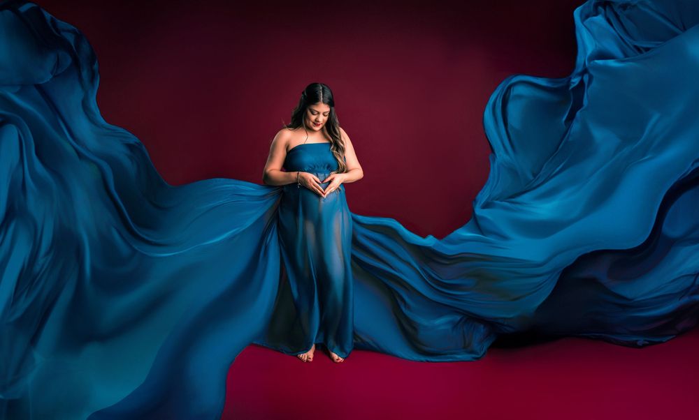 Flowing blue fabric maternity gown dramatic studio portrait against red backdrop.