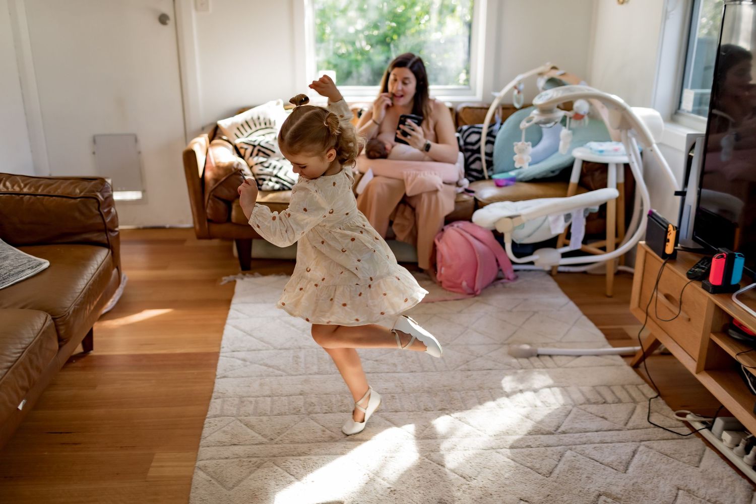 Young child dances in a sunlit living room while others watch from the couch.
