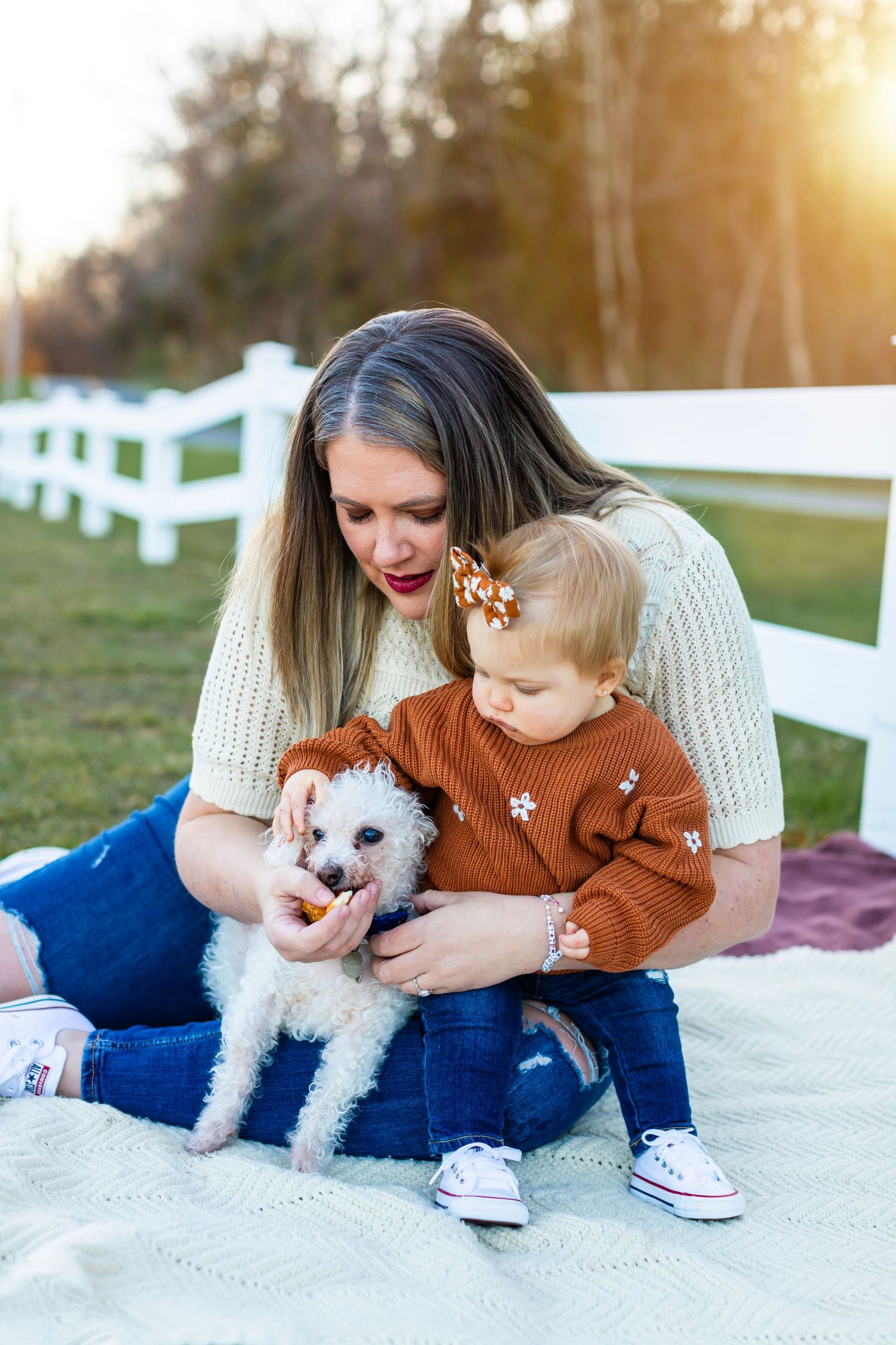 White fluffy dog sits on blanket with companions during outdoor photo session.
