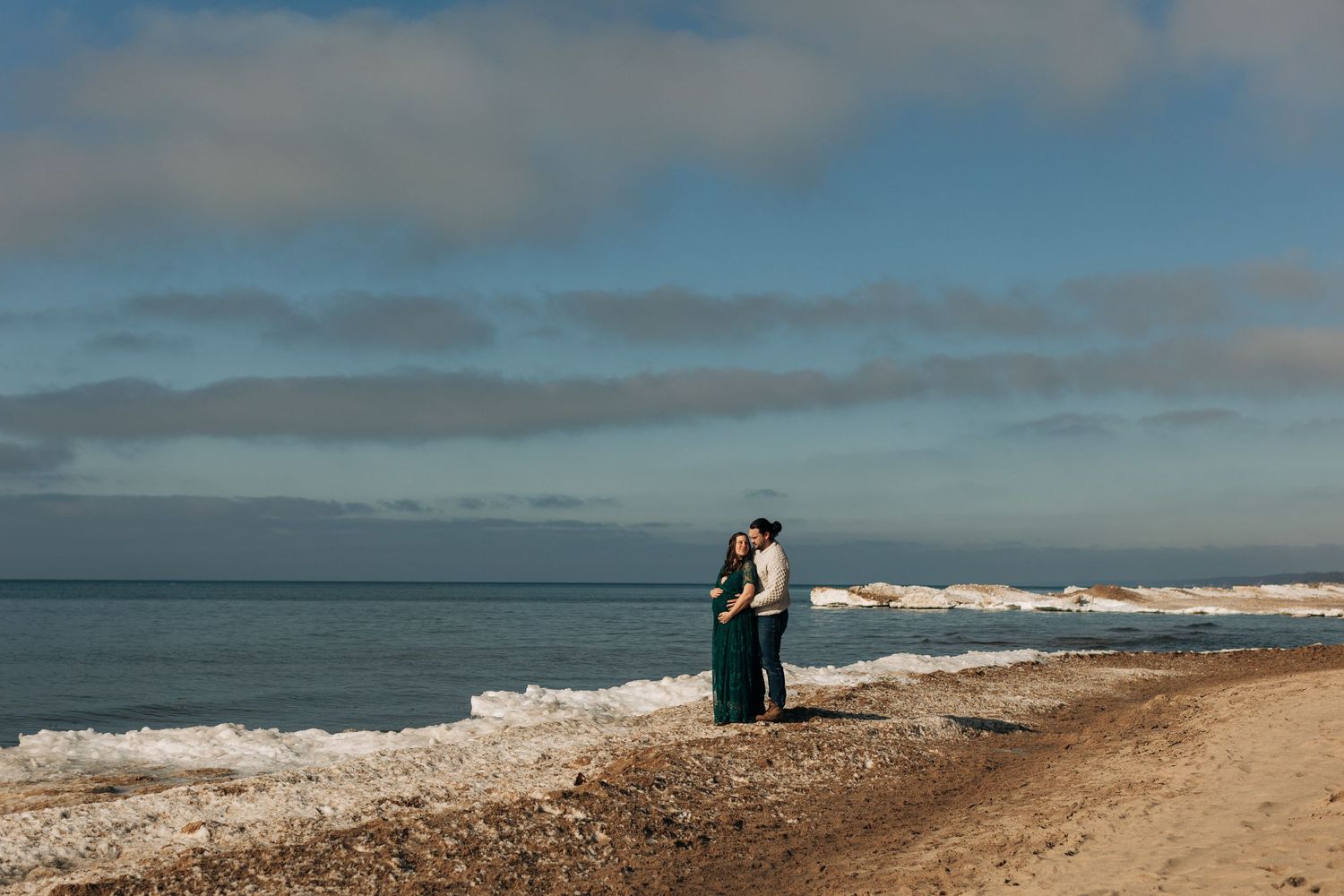 A couple embraces on a serene beach with waves crashing against the shore during a cloudy day.
