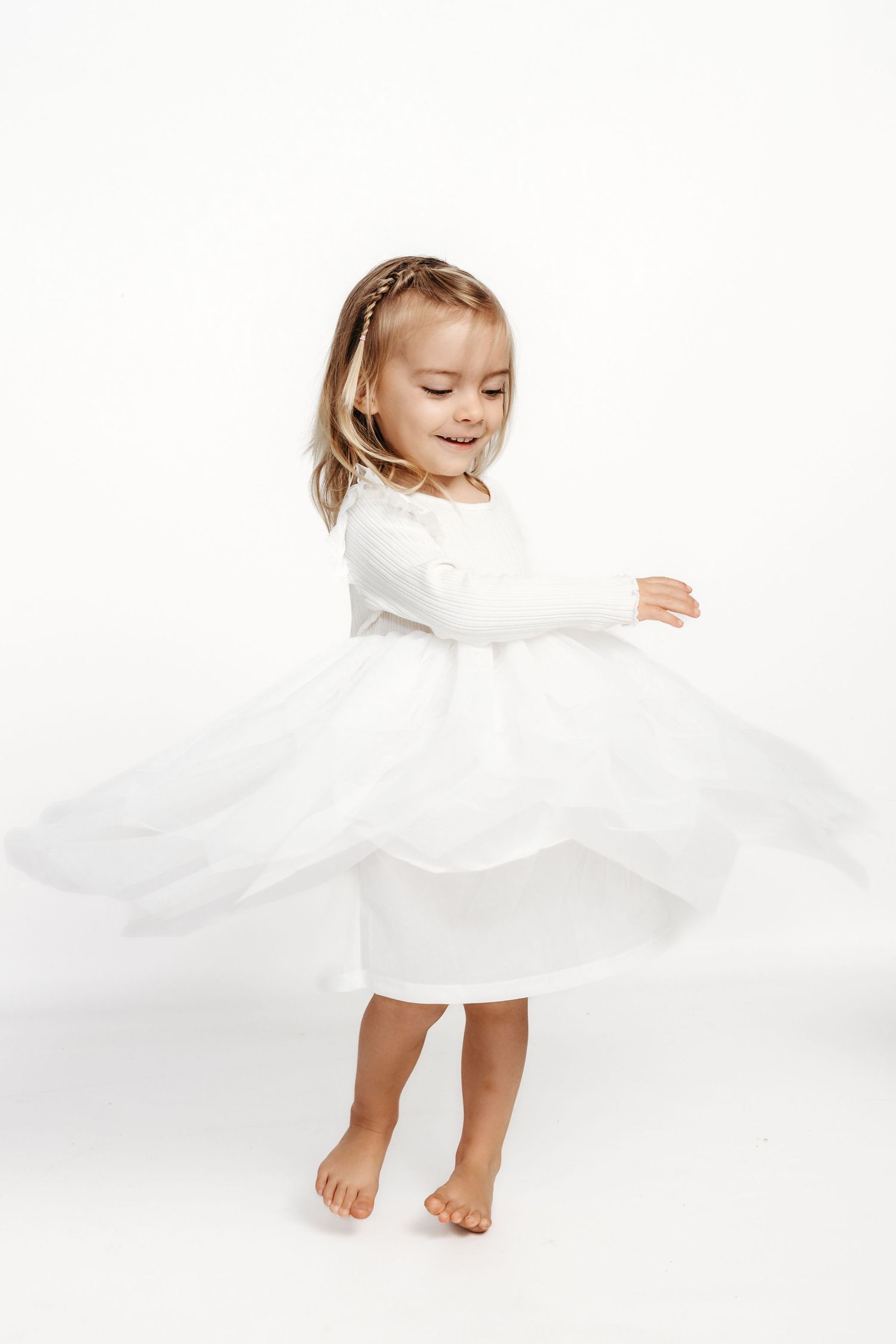 A child in a white dress twirls and dances barefoot against a white background.