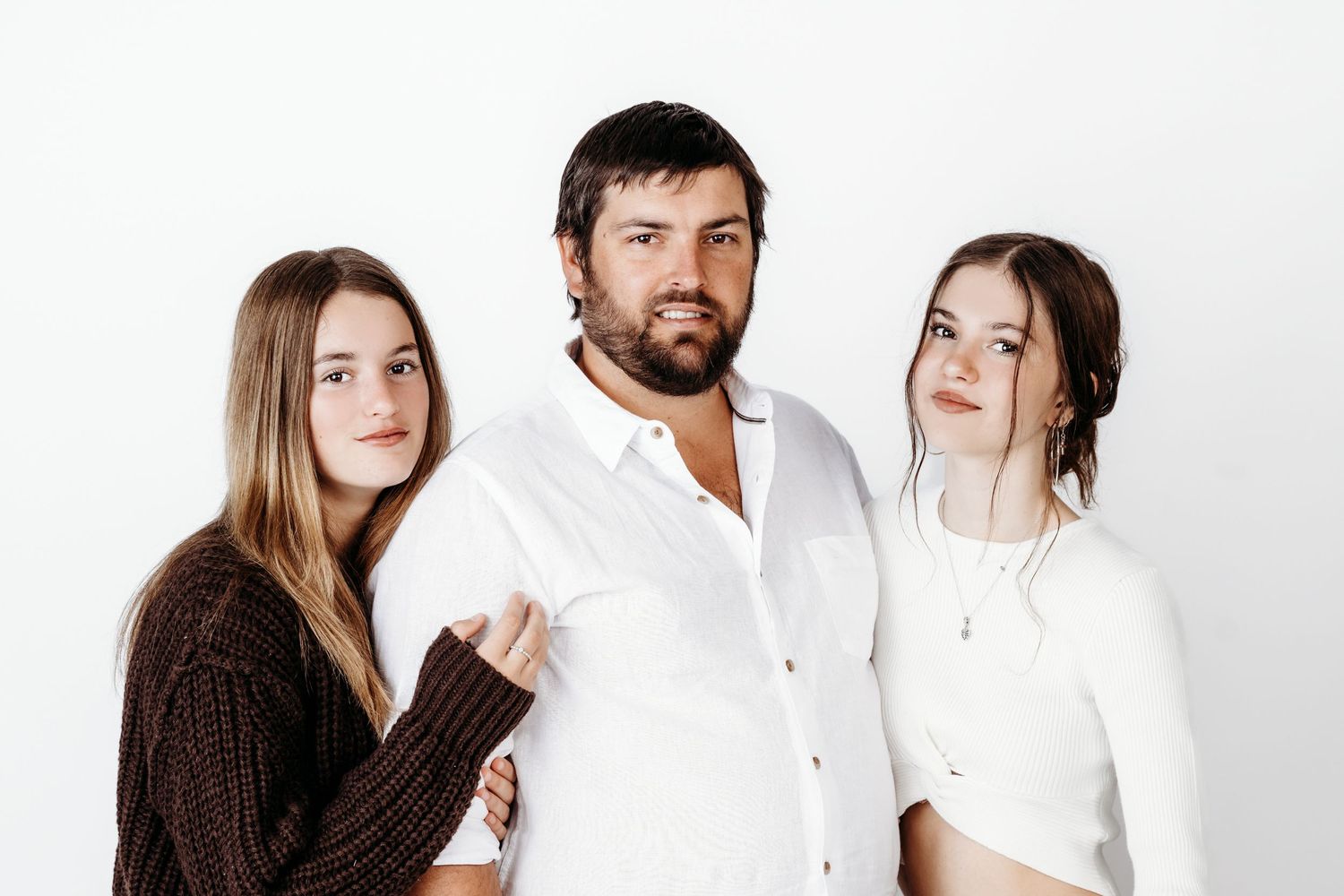 A family group poses in coordinated outfits of white and brown against a studio background.