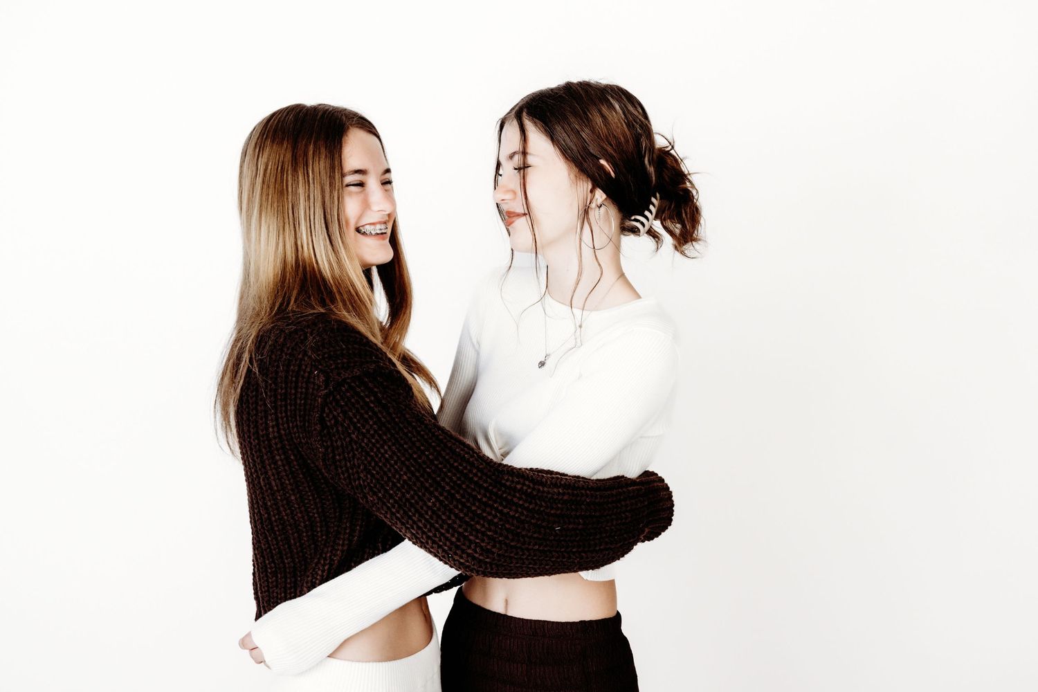 Two friends sharing a playful embrace against a white background while wearing contrasting black and white outfits.
