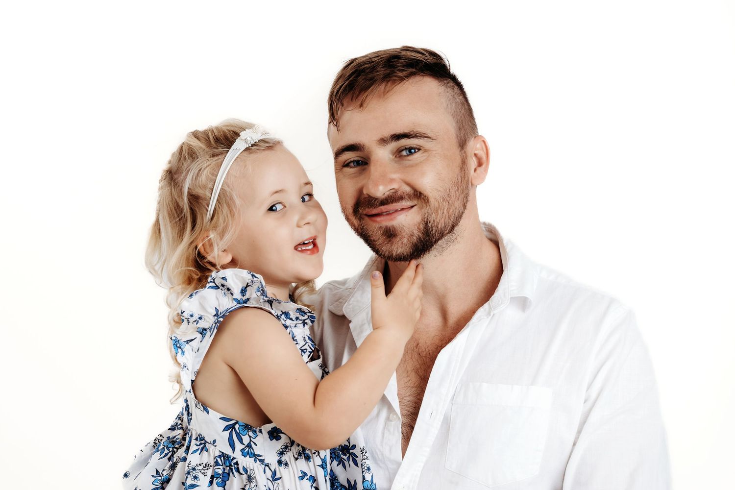 A young child in a floral dress shares a heartwarming moment with an adult in a white shirt against a white background.