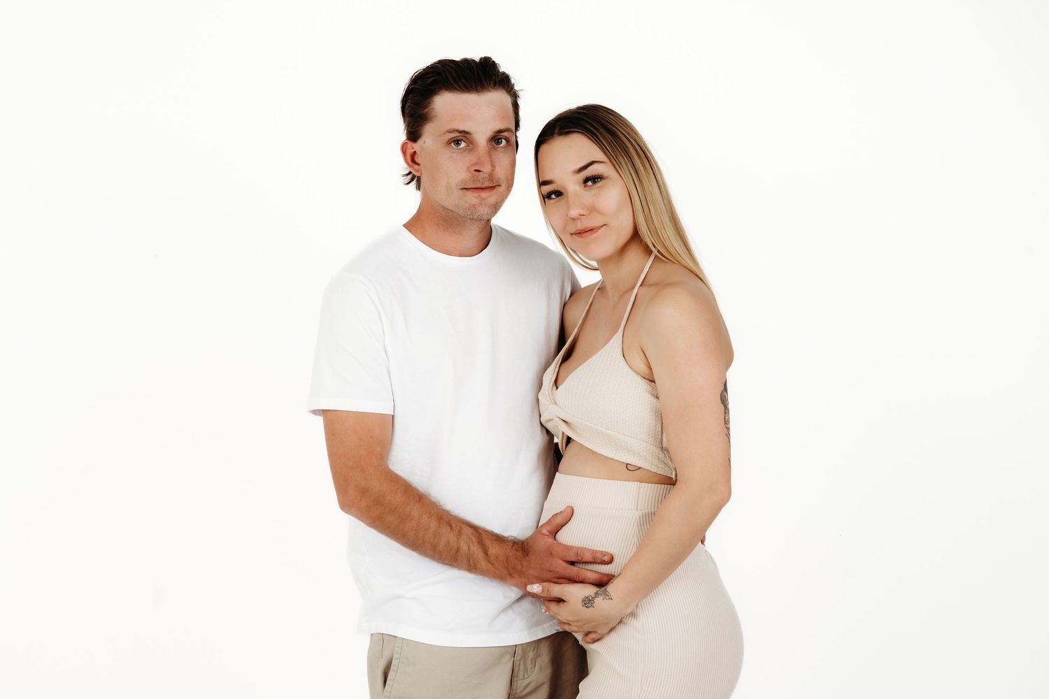 Couple in white clothing posing together against white backdrop.
