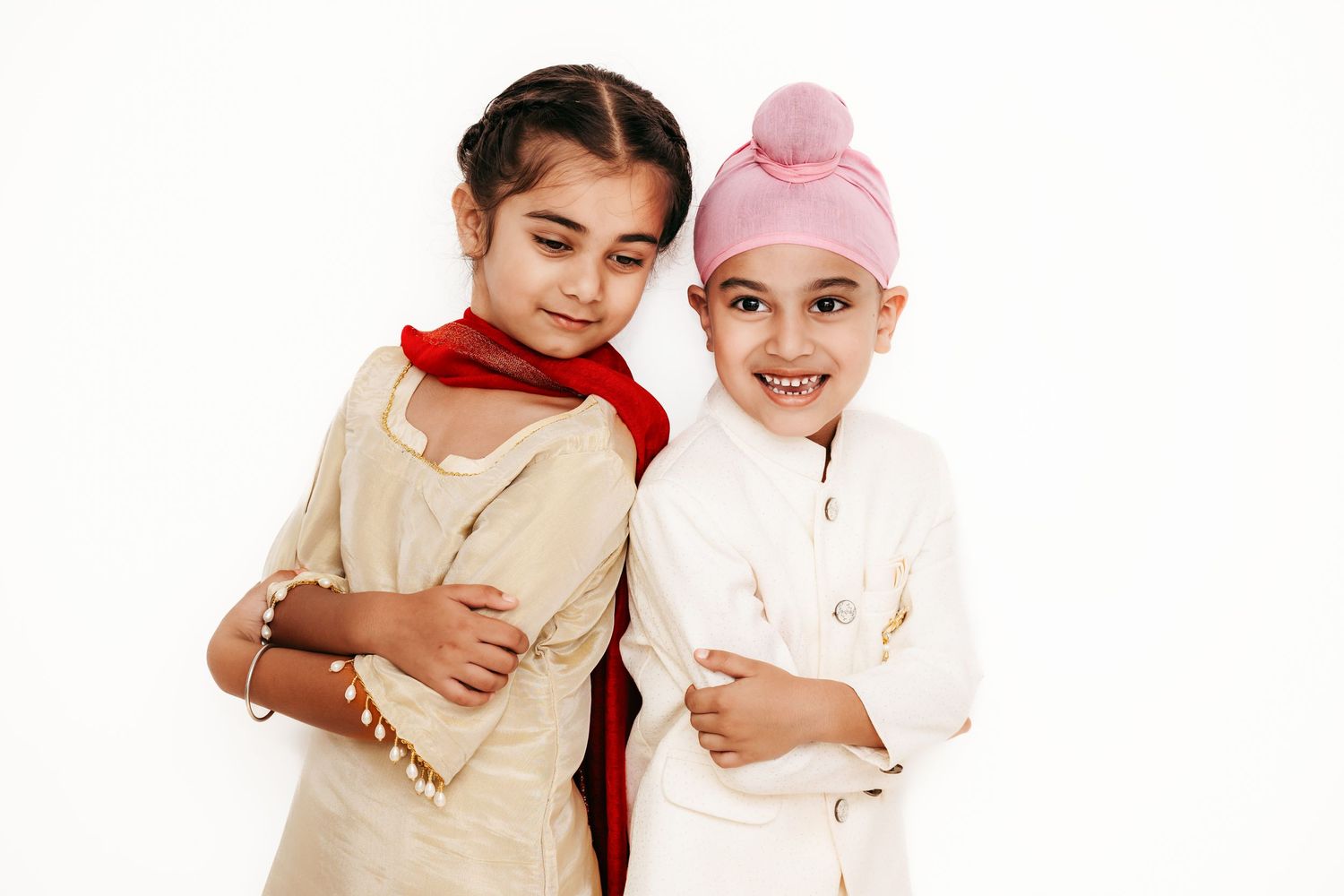 Two children in light colored outfits pose together against white background.