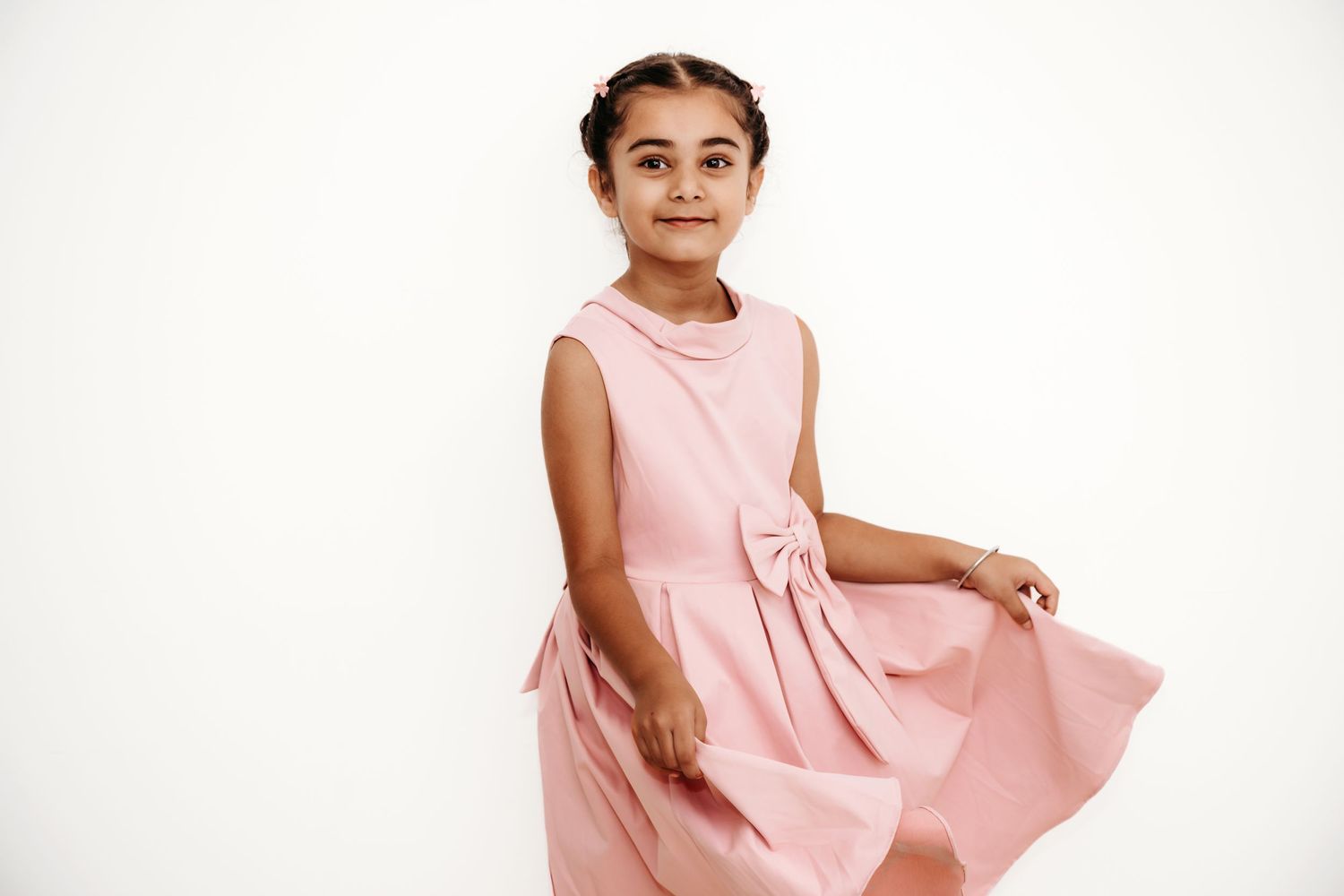 Child in pink sleeveless dress twirling against white background.