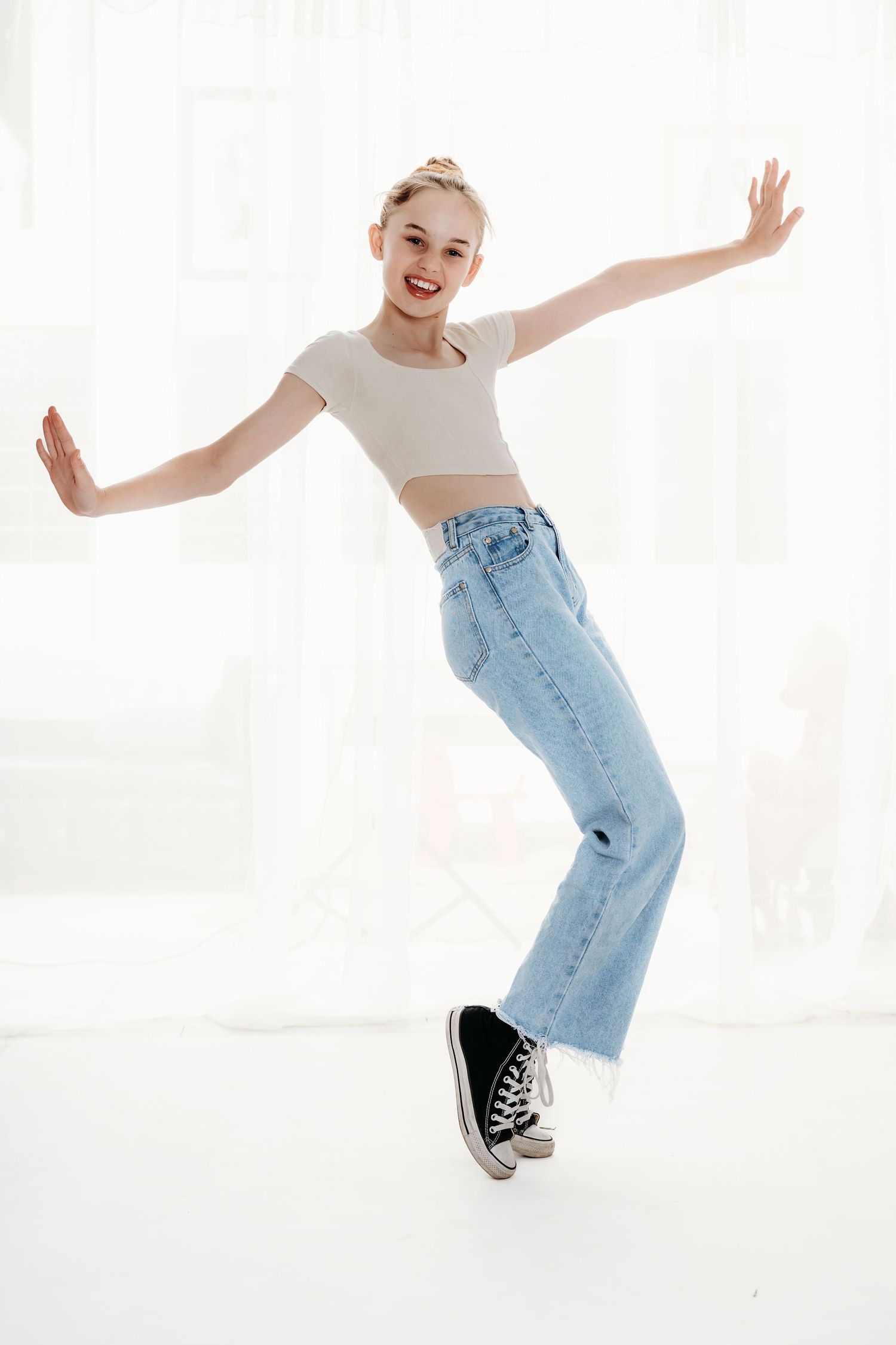 A dancer strikes an energetic pose wearing denim and a crop top against a white studio backdrop.