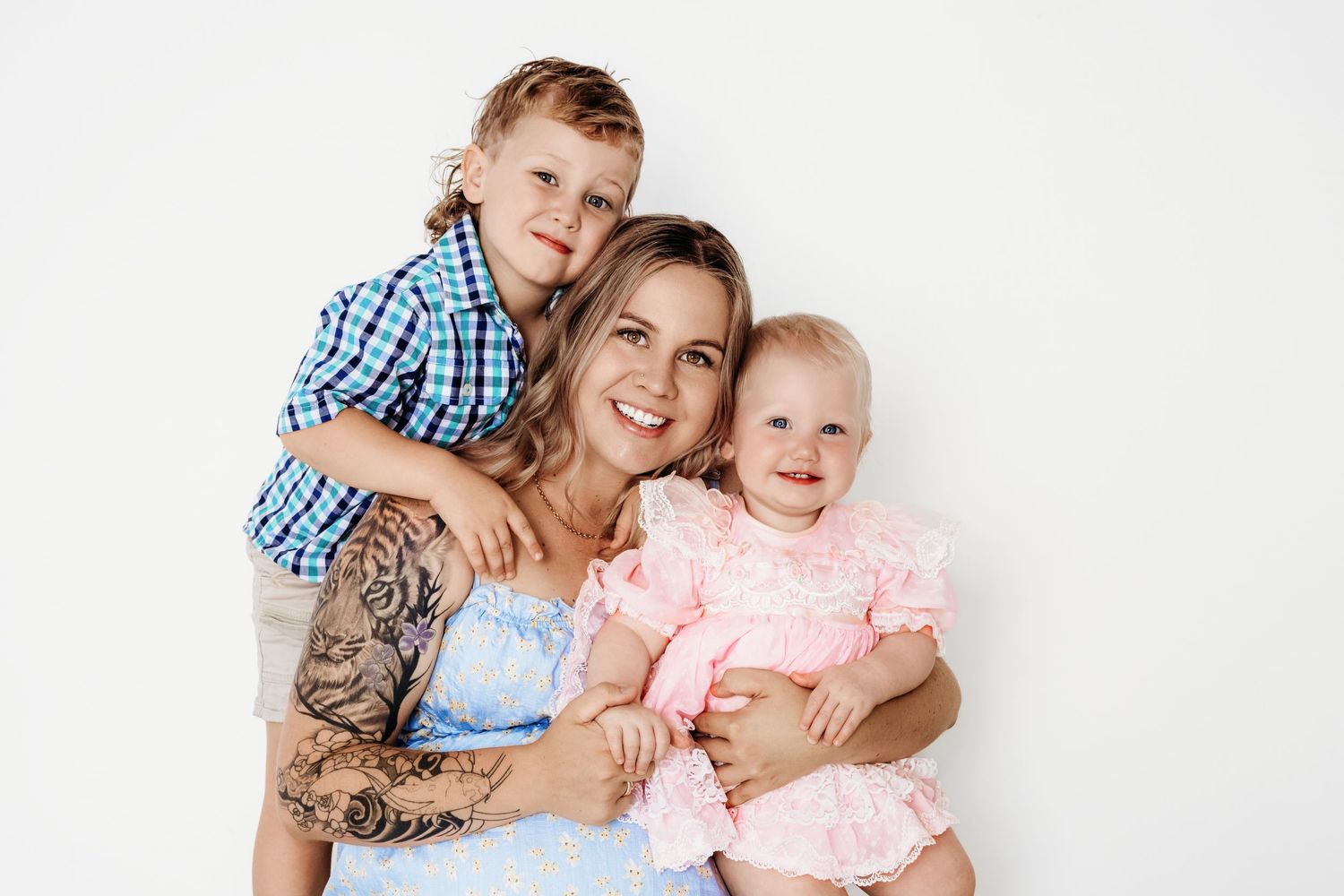 A family smiling warmly against a white background, wearing casual clothing in blue and pink tones.