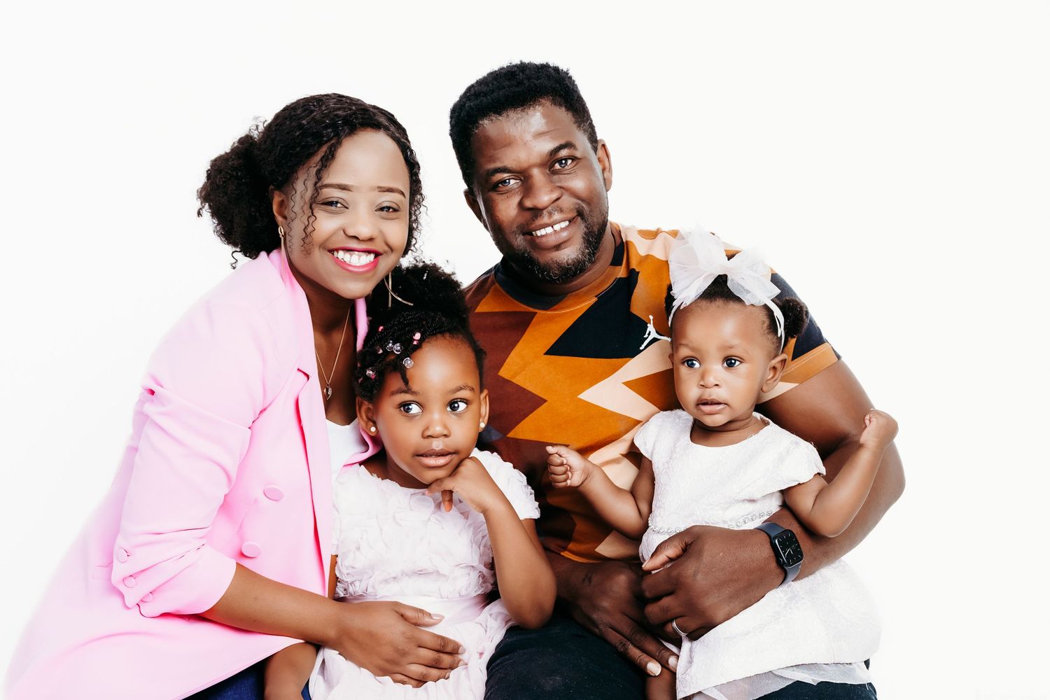 A happy family wearing pink and orange shirts poses together against a white background for a portrait session.