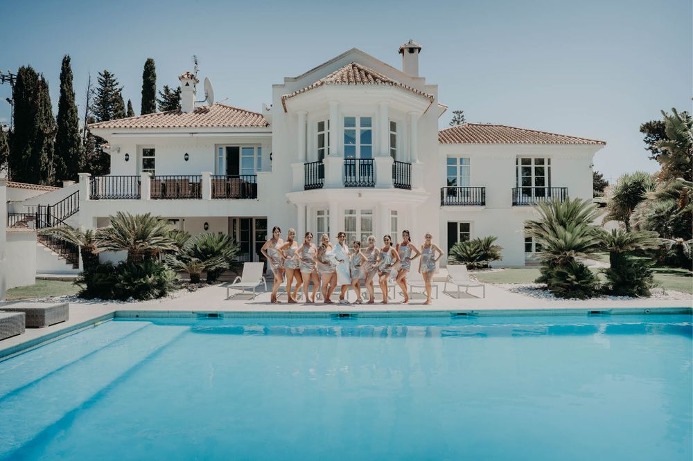 Luxurious white villa with swimming pool and wedding party group photo.