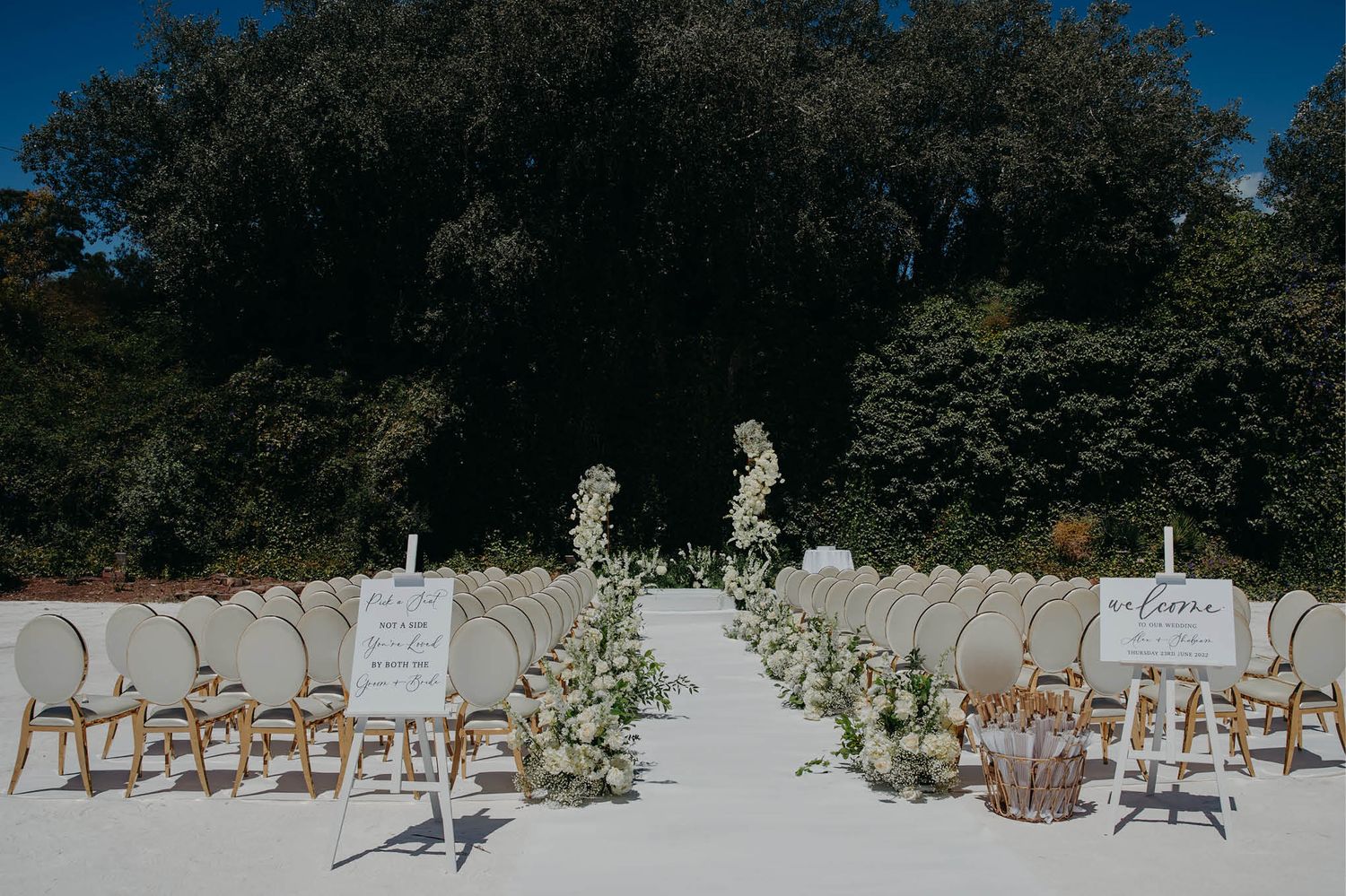 Outdoor wedding ceremony setup with white chairs and floral aisle decorations.