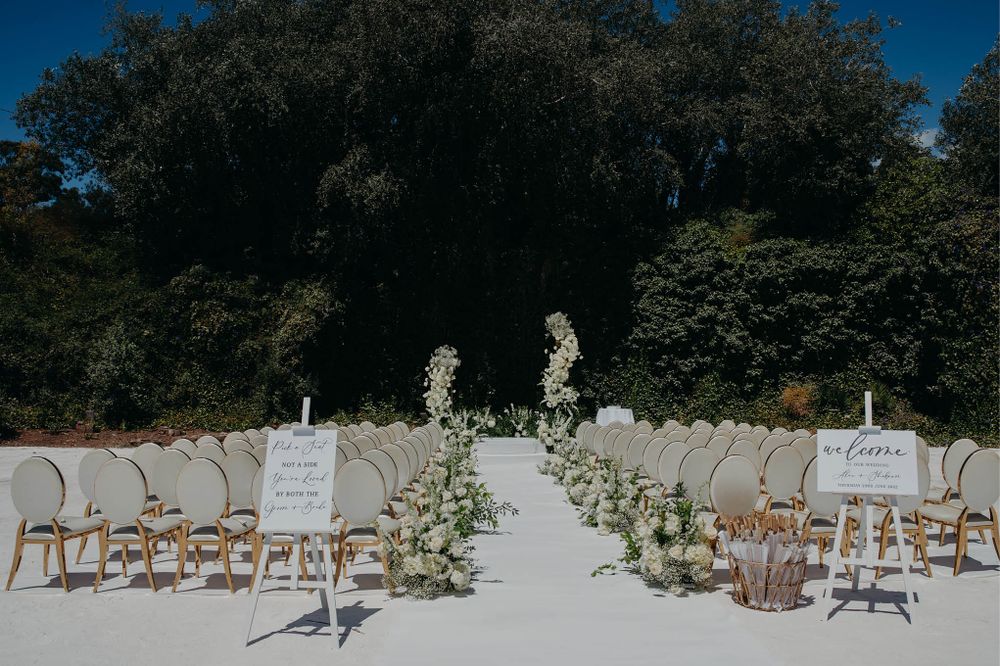Outdoor wedding ceremony setup with white chairs and floral aisle decorations.