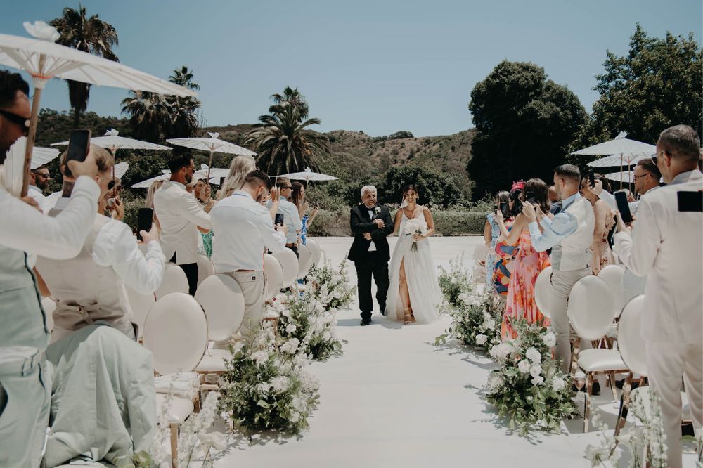 Outdoor wedding ceremony with white chairs and floral aisle decorations against a mountain backdrop.