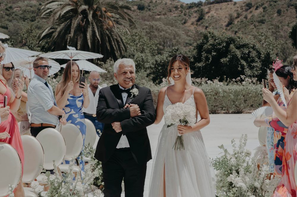 Outdoor garden wedding ceremony with guests seated on white chairs.