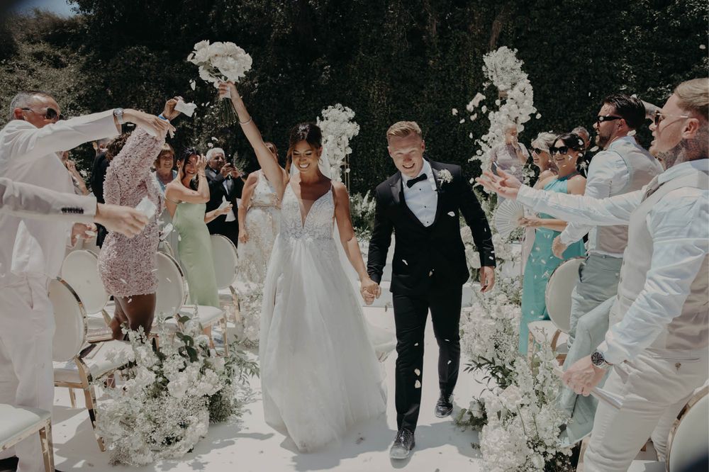 Wedding guests toss flower petals as the newlyweds walk down the aisle during their recessional.