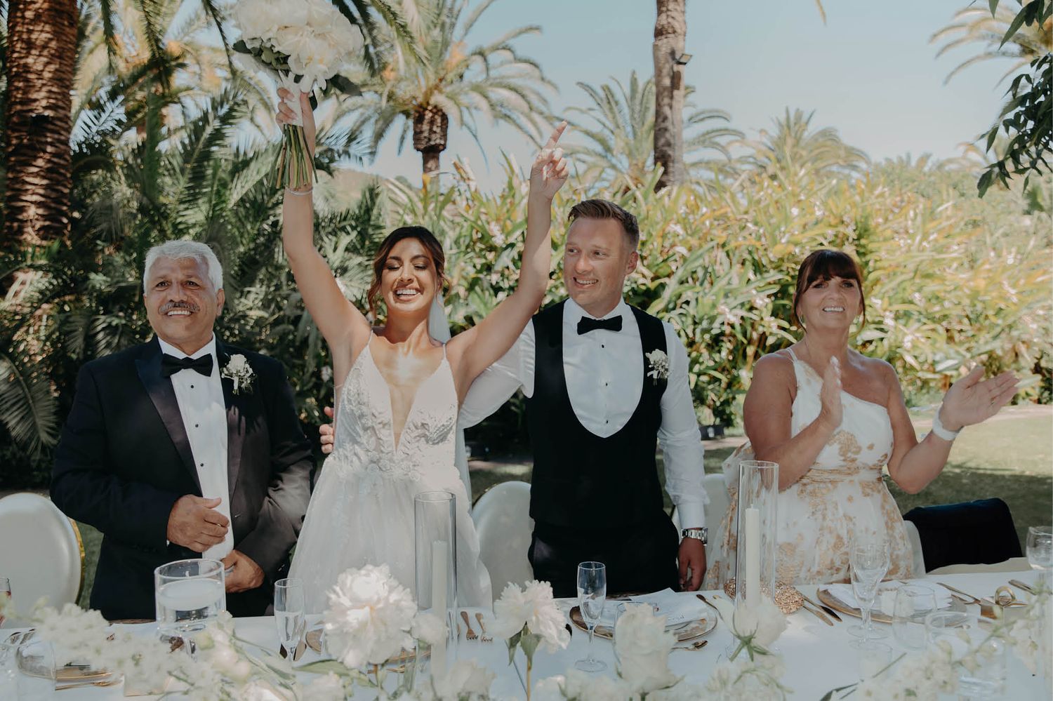 Wedding party celebrating with raised glasses at an elegant outdoor reception.