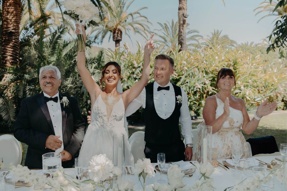 Wedding party celebrating with raised glasses at an elegant outdoor reception.