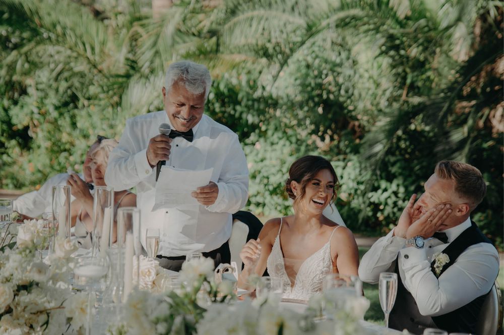 Wedding speech moment during outdoor reception with tropical garden backdrop.