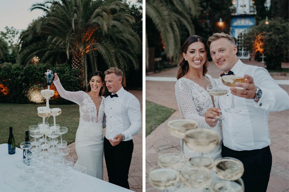 Wedding couple celebrates by a champagne tower at dusk with palm trees in the background.