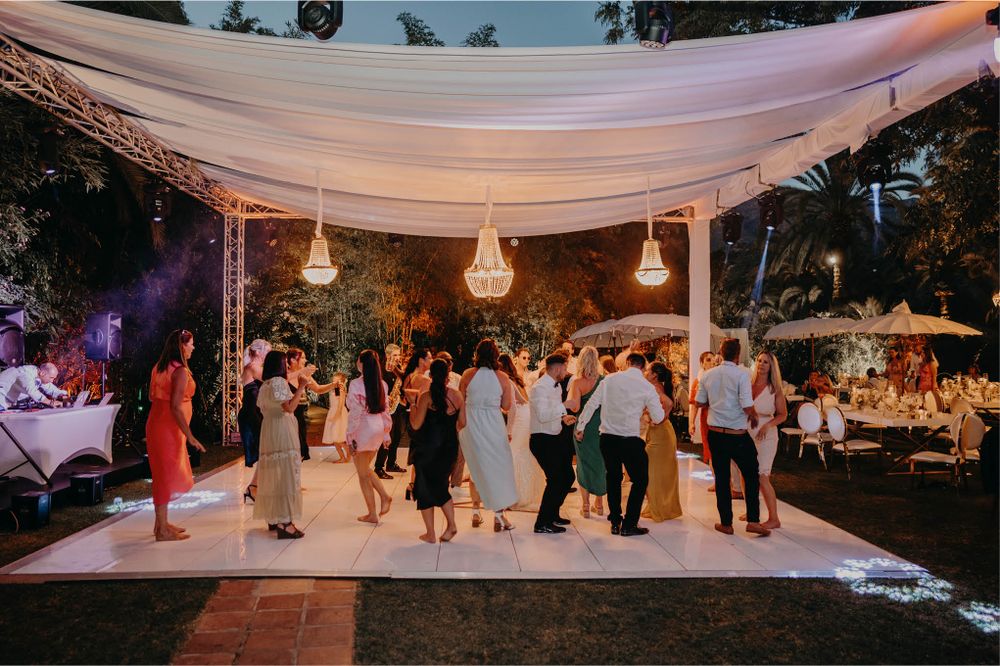 Wedding guests dancing under an elegant draped canopy with hanging lanterns at an outdoor evening reception.