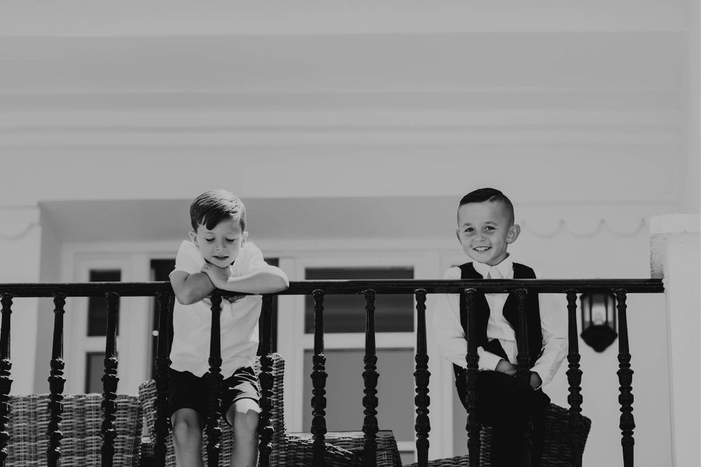 Two young children playfully peek through a wooden banister railing in black and white photography.