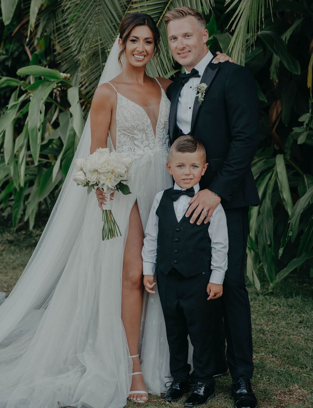 A formal wedding portrait against lush tropical foliage with elegant attire.