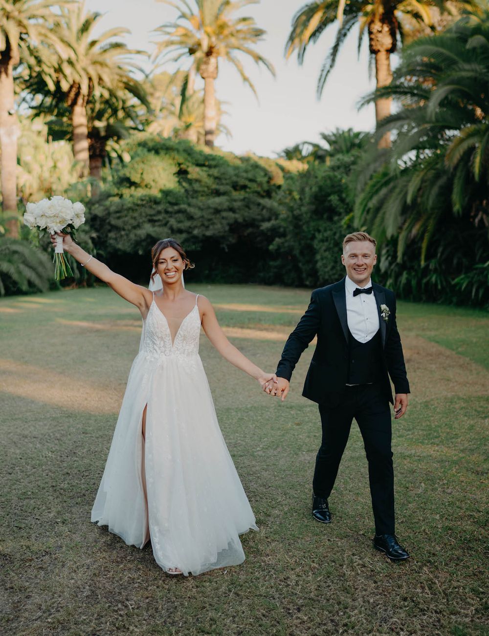 Newlyweds celebrate with joy in a tropical palm garden setting at sunset.