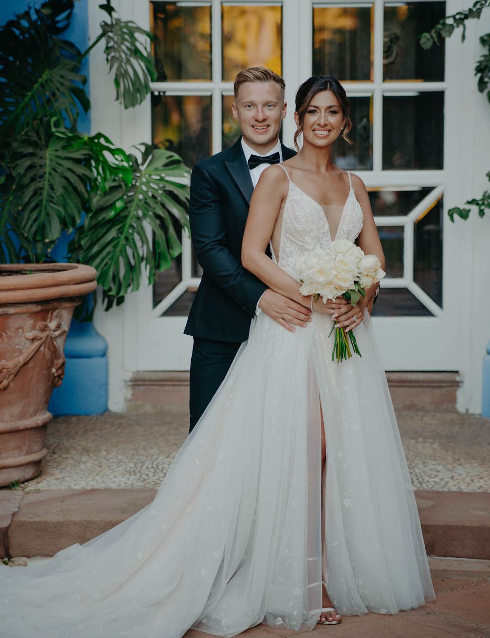 Wedding portrait of couple in elegant attire against white architectural backdrop.