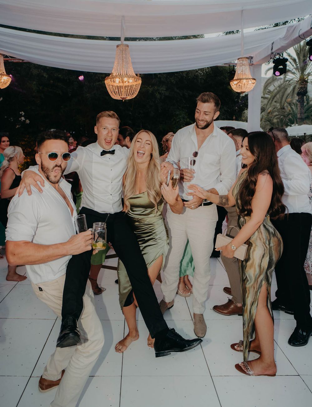 Wedding reception party on dance floor with chandeliers and white draping.