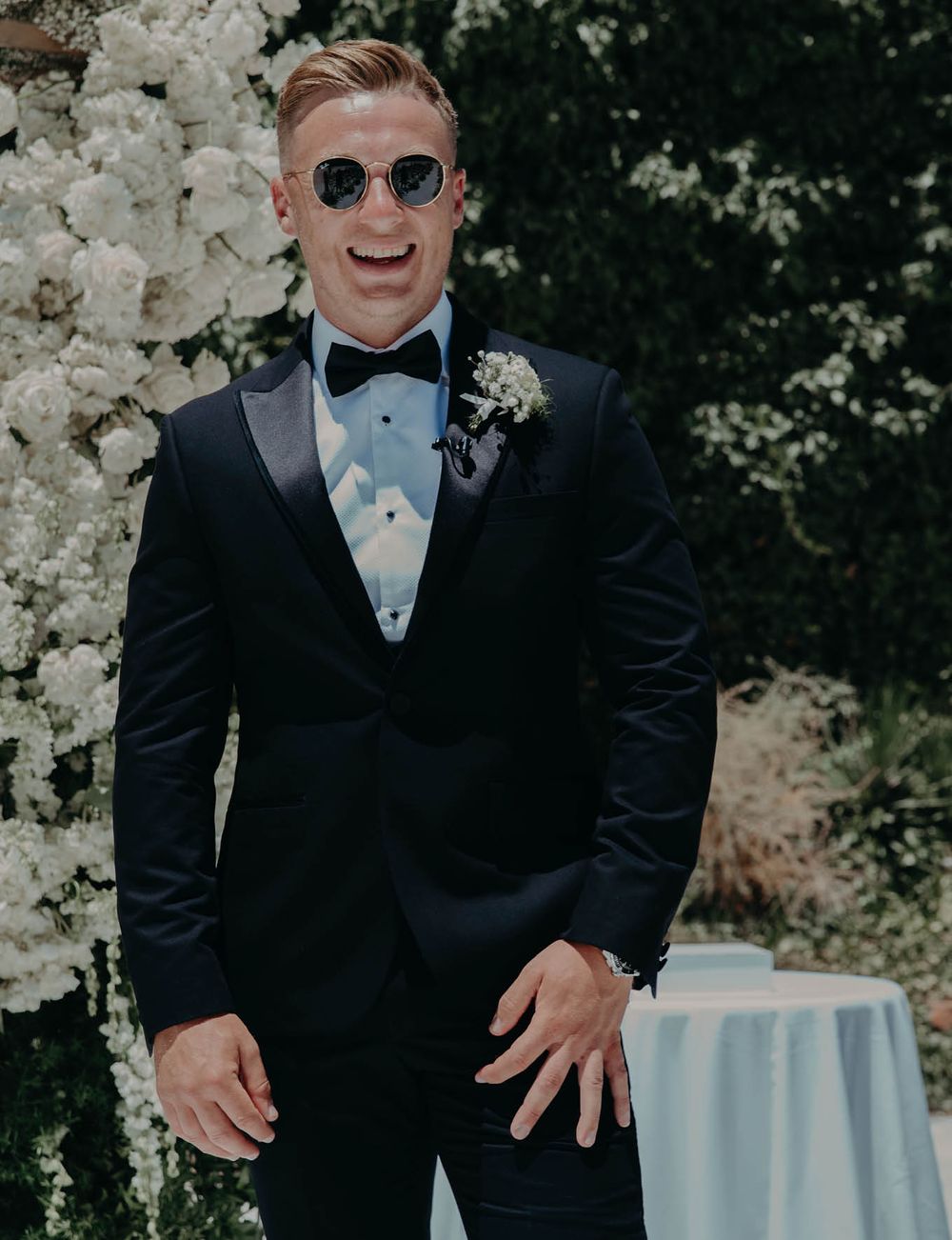 A formal portrait against white floral decorations at an elegant outdoor wedding.