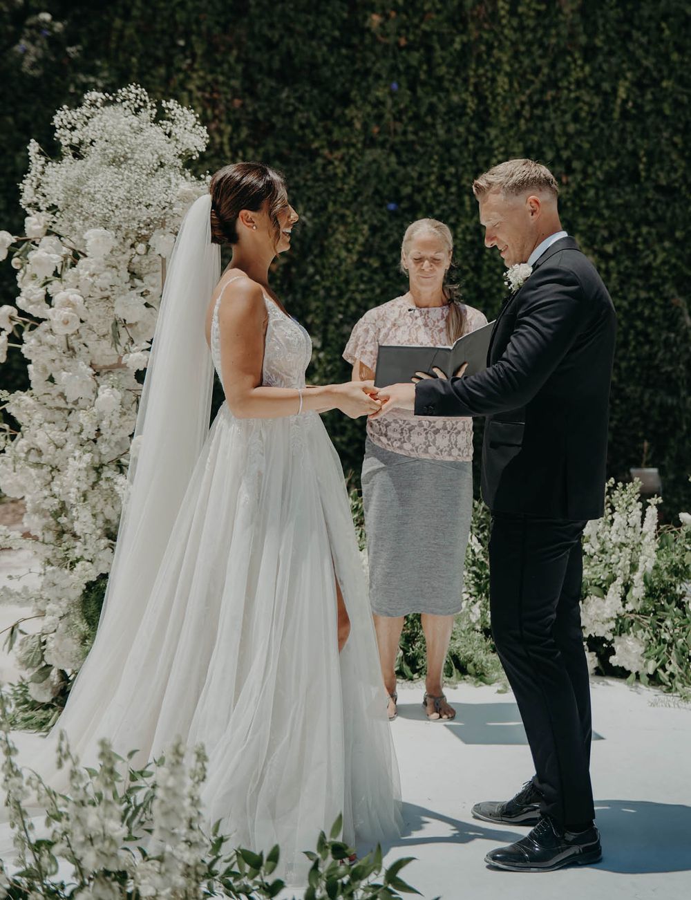 An outdoor wedding ceremony with white floral arch and elegant garden setting.