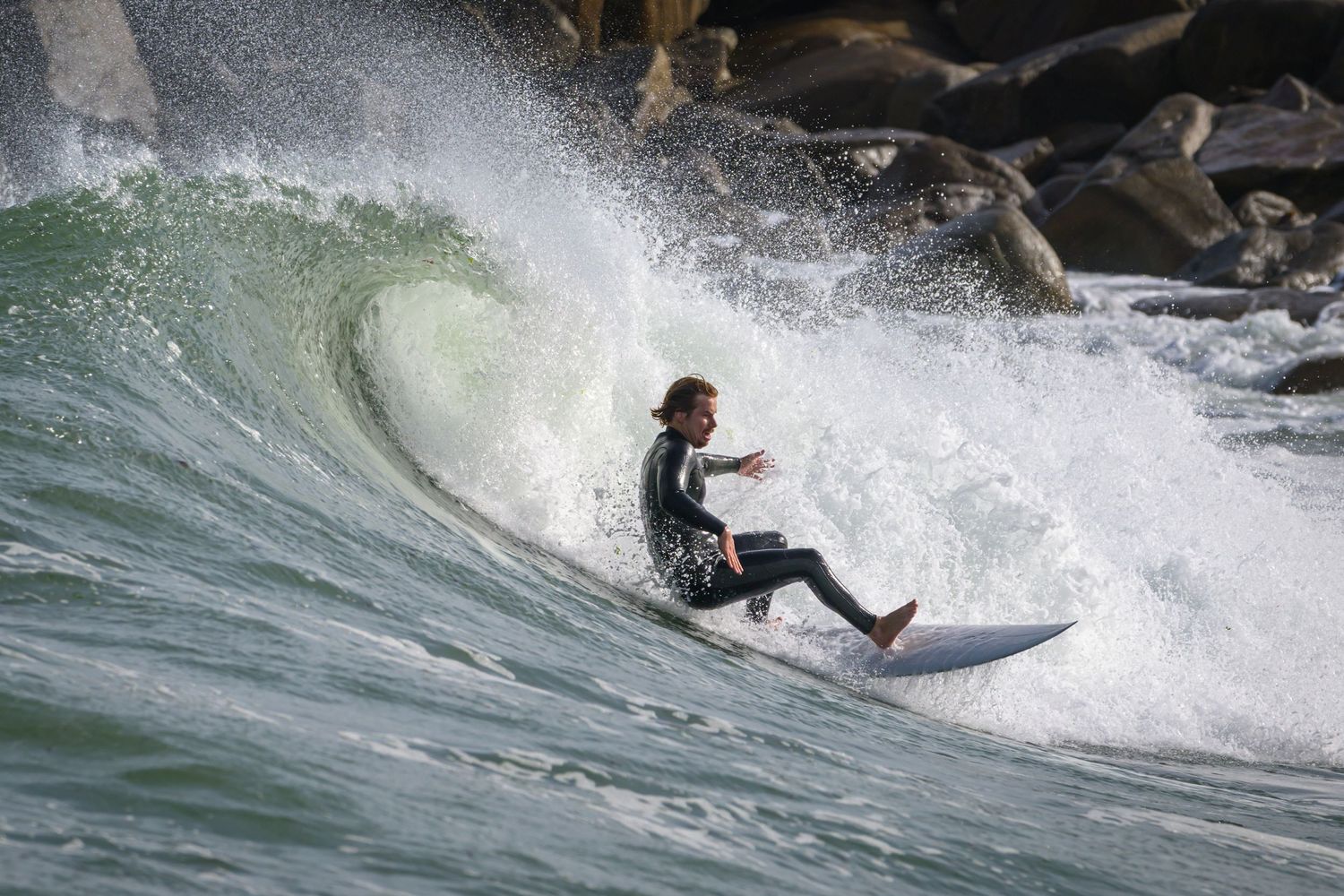 Surfer navigating down steep face of large breaking ocean wave.
