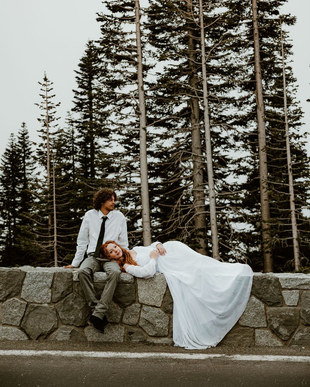 A romantic wedding photo sequence showing a couple lounging on a stone wall surrounded by evergreen trees.