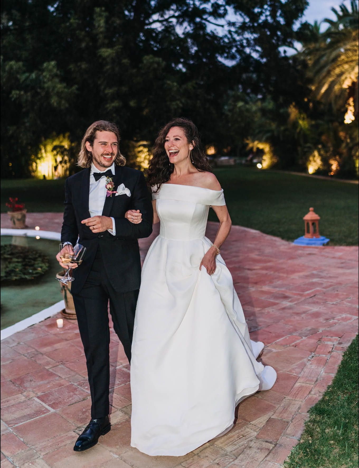 Newlyweds share a joyful moment while walking on a terracotta pathway.