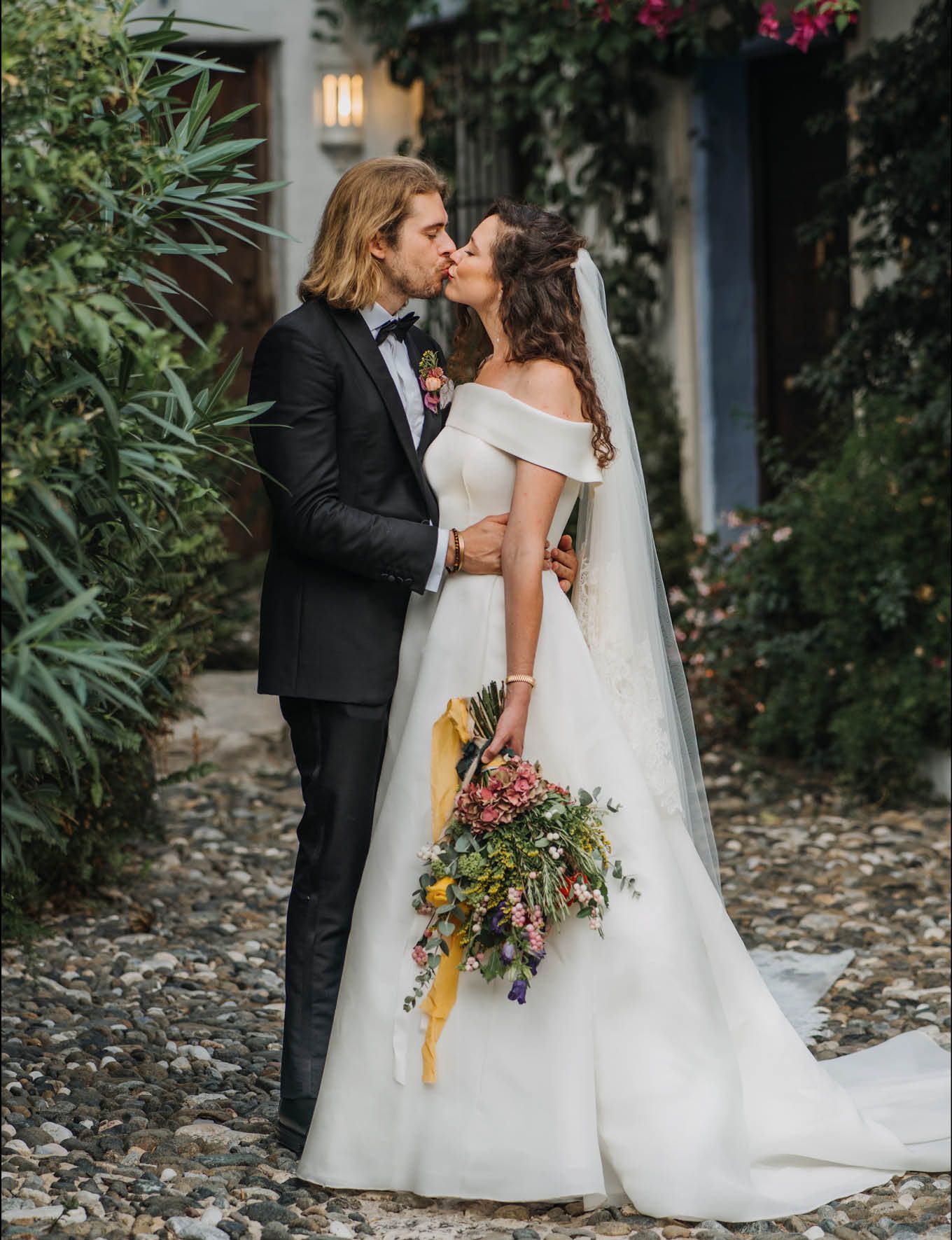 Intimate wedding couple moment on stone path surrounded by lush greenery.