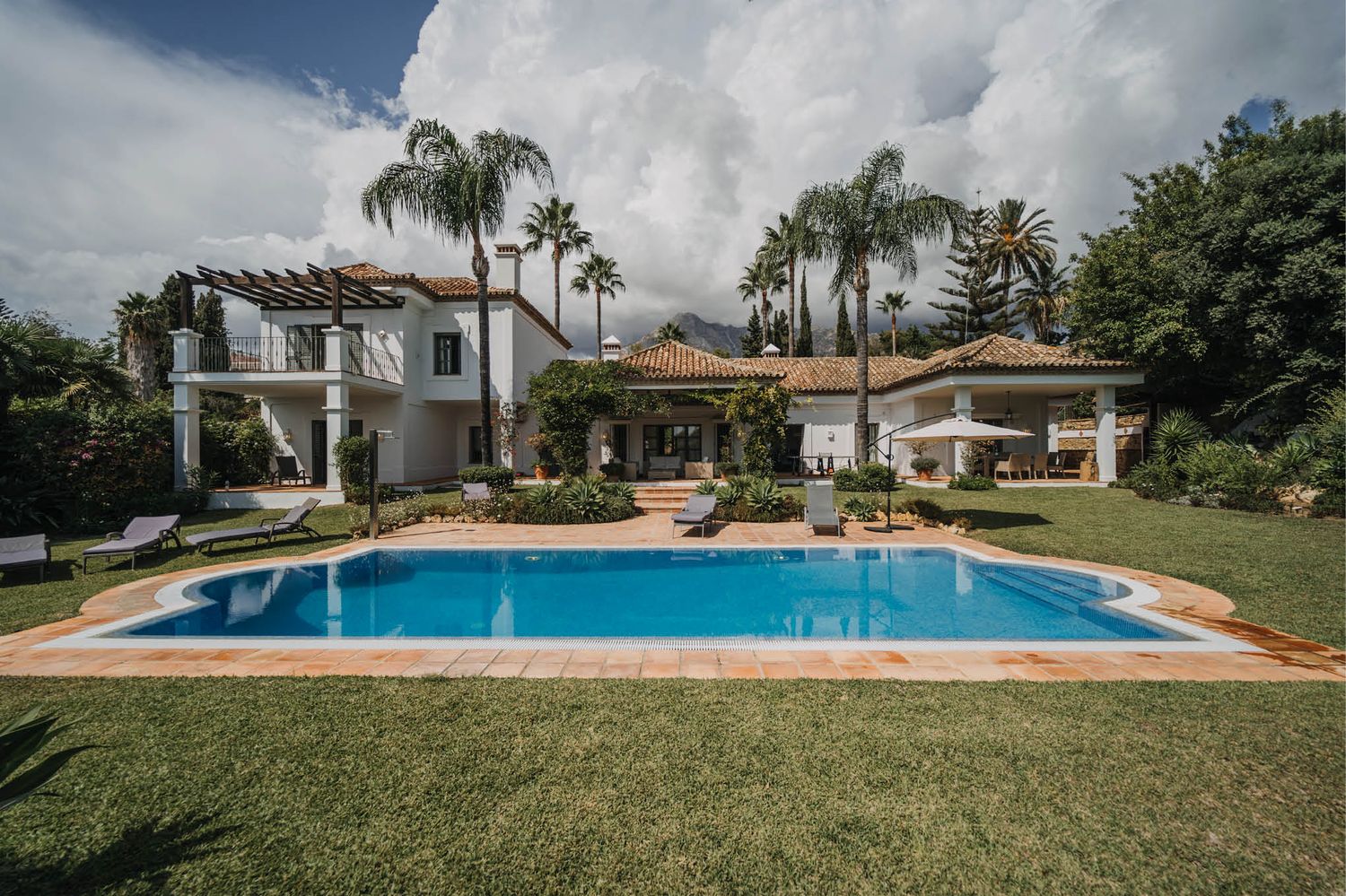 Luxurious white villa with swimming pool surrounded by palm trees and lush landscaping.