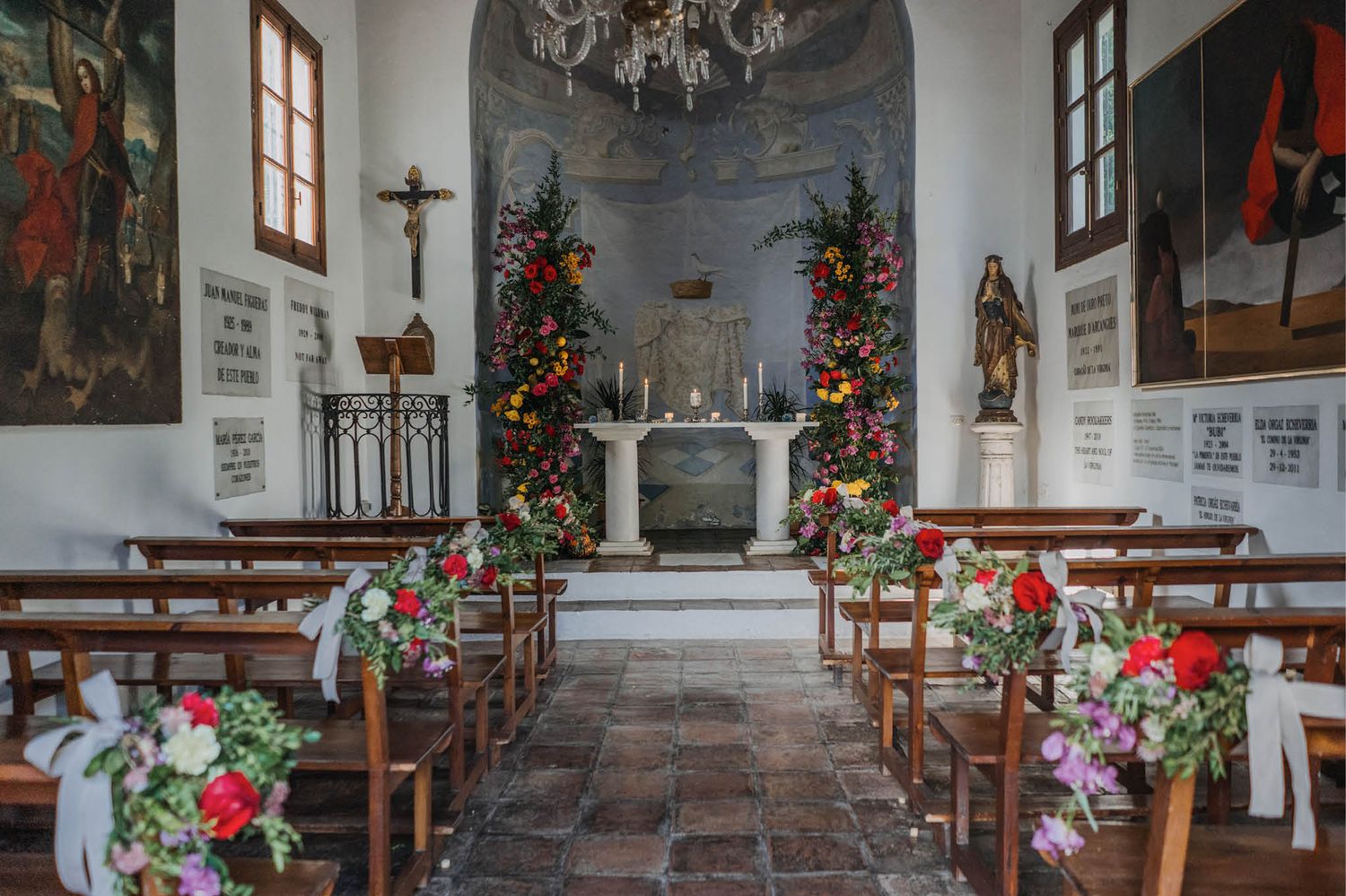 Small church interior decorated with red floral arrangements and wooden pews for a wedding ceremony.