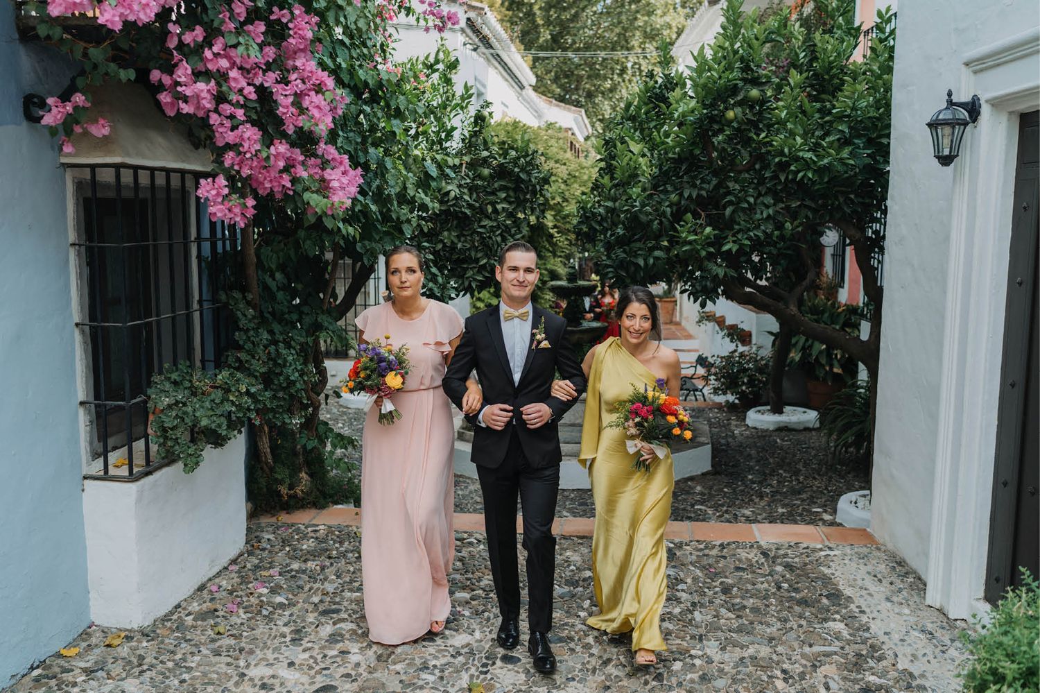 Wedding party members in pastel dresses walking down a garden pathway.